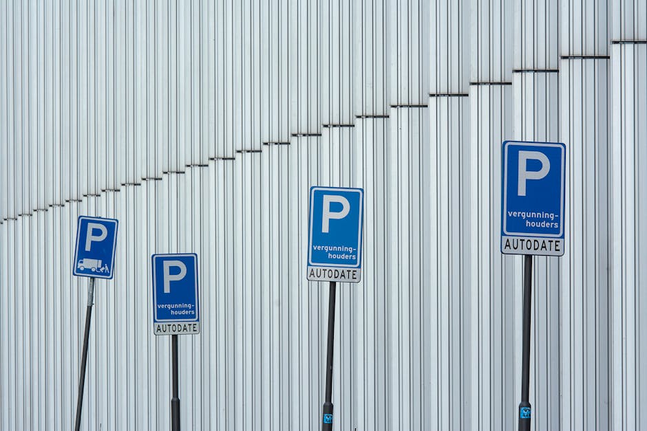 Four blue parking signs with the letter 'P' and the text 'vergunninghouders' and 'AUTODATE' are mounted on thin black poles in front of a metallic corrugated wall. The signs are positioned along the pavement, with the largest sign placed directly in front of the wall, and the others slightly tilted, indicating designated parking areas for permit holders near a property. The wall's surface features vertical ridges that reflect ambient light, creating a subtle shine. The area appears well-lit, with soft shadows cast by the signs. This image relates to house removals and moving services, highlighting the importance of understanding local parking regulations on move day, which Putney Man and Van can assist with during furniture transport and home relocation processes.